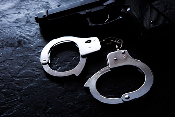 Black steel gun and Police metal real handcuffs lie on the black background. Private detective...
