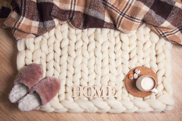 Fototapeta na wymiar Home fur slippers, cup of cappuccino and cookies, checkered plaid on the blanket of thick yarn with copy space