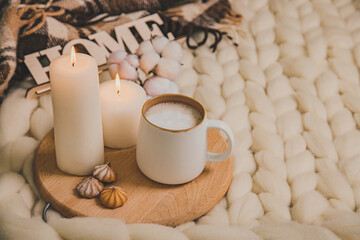 Cup of cappuccino and cookies, candles, checkered plaid, inscription Home on the background of blanket of thick yarn.