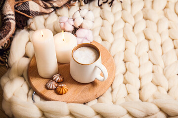 Cup of cappuccino and cookies, candles, checkered plaid on the background of blanket of thick yarn.