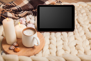 Mockup tablet with Cup of cappuccino and cookies, candles, checkered plaid on the background of blanket of thick yarn.