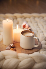 Fototapeta na wymiar Cup of cappuccino, cookies, and candles on the background of blanket of thick yarn.
