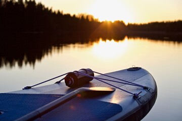 Paddle board and surf board with paddle in sunset light on water background close up. Surfing and SUP boarding equipment in sunset lights close-up. Outdoor water sports. Surfing lifestyle backgrounds.