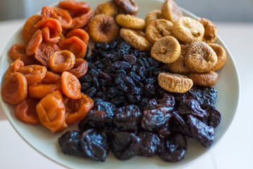 Men's hands hold a plate of dried fruit over the table. Prunes, dried apricots, figs, raisins on a large platter.