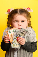 Caucasian girl holding money, portrait of a child on a yellow background, financial literacy of children.