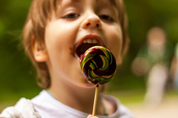 Portrait of a cute little boy holding a large round lollipop. The baby eats a sweet, big lollipop.