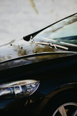 Black color car windshield wiper close-up with  front windscreen and car hood.