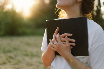 Woman holds book in her hands. Reading the book in a field during sunset.
