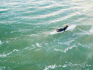 Aerial view of a lone surfer paddling a board on the ocean