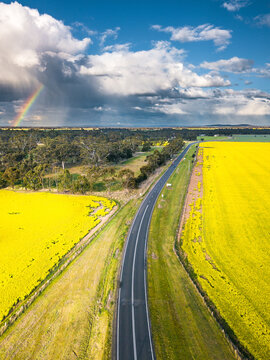Aerial view of a country road running through farmland with clouds and a rainbow in the distance