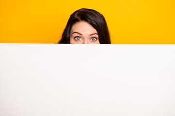 Photo of funny cute young lady dressed white t-shirt hiding white bill board empty space isolated yellow color background