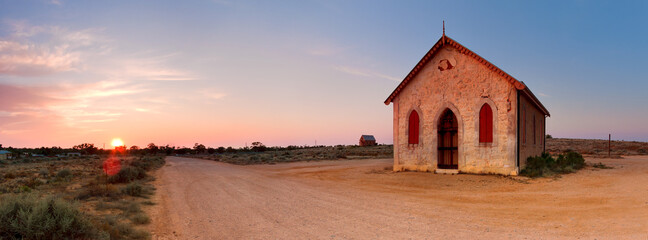 An isolated chapel beside a dirt road as the sun rises