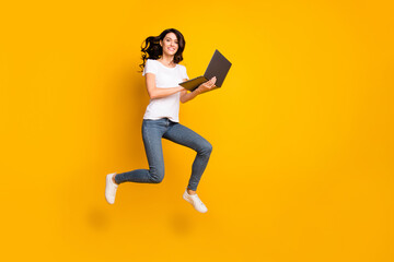 Fototapeta na wymiar Full length body size view of lovely cheerful girl jumping using laptop success isolated over bright yellow color background