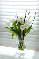 Beautiful bouquet of willow branches and tulips in vase near window
