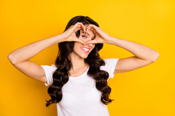 Naklejka premium Portrait of attractive cheerful wavy-haired girl showing heart shape sign isolated over bright yellow color background