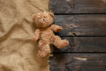 an old teddy brown bear lies alone on a charred wooden floor on a brown cloth, a child's toy