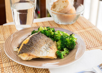 fried fillet of sea bass with garnish of broccoli on black warm stone plate