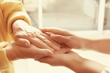 Helping hands on blurred background, closeup. Elderly care concept