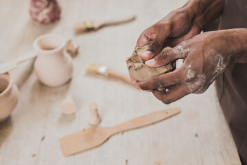 partial view of young african american man sculpting piece of clay with hands near table with equipment in pottery