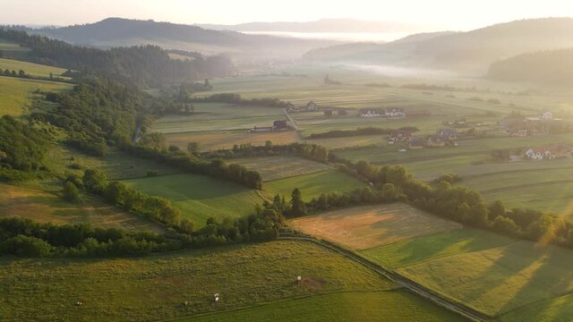 Aerial drone fly over farm fields and Kacwin village in Polish mountains at sunrise. Morning fog over landscape