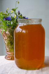 Glass jar with natural honey on the kitchen table. Vase with Flowers. Vertical image. 