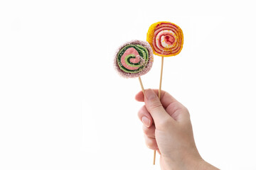 Person holds two colorful lollypops on wooden sticks in hand on white background