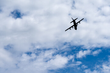 Fototapeta na wymiar silhouette of an old four propeller airplane against a backdrop of white clouds and blue sky