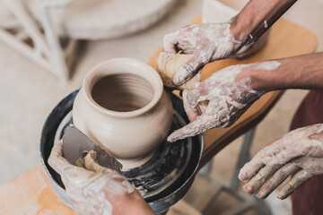 close up view of young african american couple shaping wet clay pot on wheel with hands and scraper in pottery