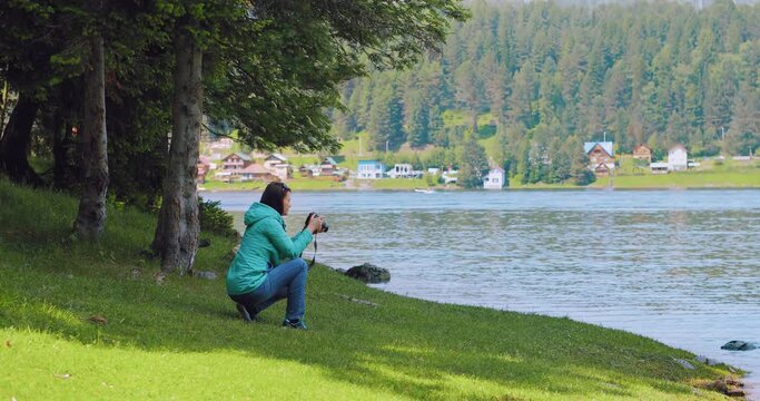 A girl photographer is squatting on the shore of a beautiful lake. She holds a digital camera in her hands and takes pictures of nature. A girl takes pictures of a beautiful landscape.