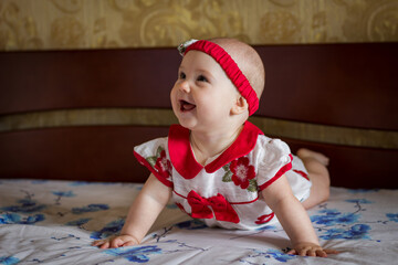 Toddler baby with red ribbon laughing on the bed at home