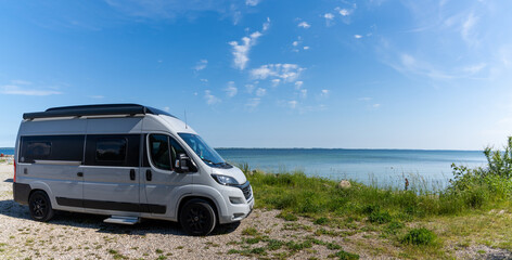 gray camper van parked next to a picturesque shore with turquoise water and forest under a blue sky