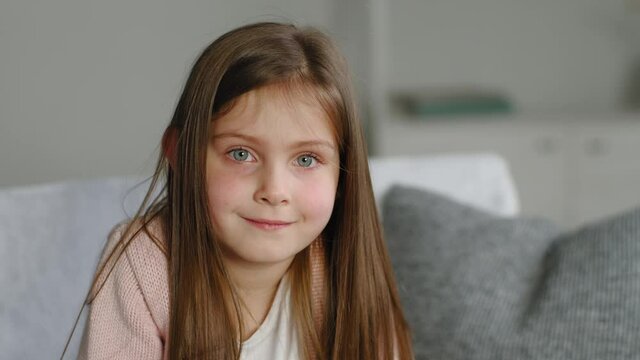 Portrait pretty caucasian child kid baby toddler school girl looking at camera indoors, adolescent funny cute little small model with beautiful face and blue eyes smile posing at home sitting on couch