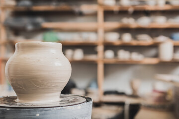 wet clay pot on pottery wheel on wooden bench in art studio