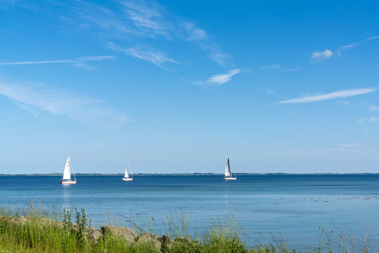 three sailboats sailing off the shore of Denmark with clear with turquoise water in the foreground