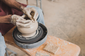 partial view of male african american hands shaping wet clay pot on wheel near sponge and scraper...
