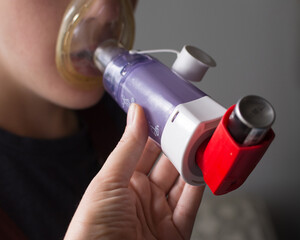 Young boy using asthma inhaler with help from parent; a spacer is used to help child take medication - obrazy, fototapety, plakaty