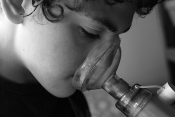 Young boy taking asthma inhaler medication using a spacer and mask - obrazy, fototapety, plakaty