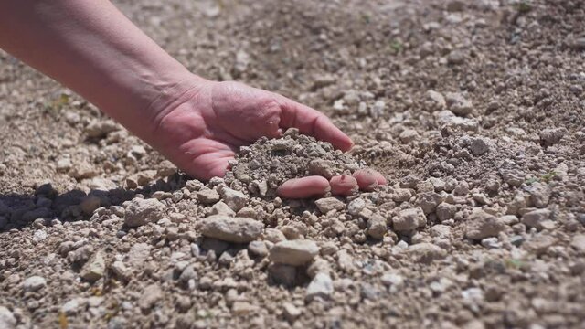Closeup view  4k stock video footage of female hand holding and touching grey dry hot soil outdoors on sunny hot summer day
