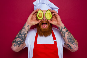 happy chef with beard and red apron holds an avocado