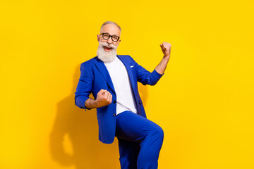 Photo portrait of bearded man in spectacles blue suit gesturing like winner isolated bright yellow...
