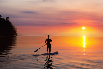 Adventurous woman on a paddle board is paddeling in the Pacific West Coast Ocean. Sunset Sky Art Render. Taken near Spanish Banks, Vancouver, British Columbia, Canada.