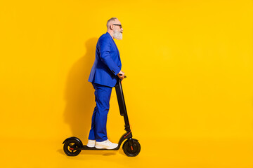 Full size profile side photo of mature businessman riding ecological scooter isolated on yellow color background © deagreez