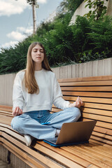 A young student girl sits in an urban park in the city and meditates during a break before studying science. University campus, education and study in the open air.