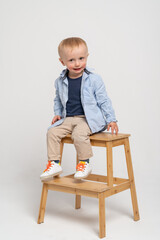 Little boy on the white background making funny face - blonde caucasian child sitting on the wooden ladder