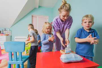 Lovely kindergarten kids cleaning hands with sanitazer