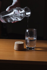 pours water into a glass from a glass bottle