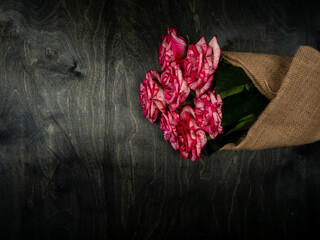 Fresh, red roses lie in burlap, on a black wooden background. Flower rose close up. Postcard.