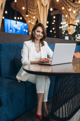 Beautiful Young Freelancer Woman Using Laptop Computer Sitting At Cafe Table. Happy Smiling Girl Working Online Or Studying And Learning While Using Notebook. Freelance Work, Business People Concept