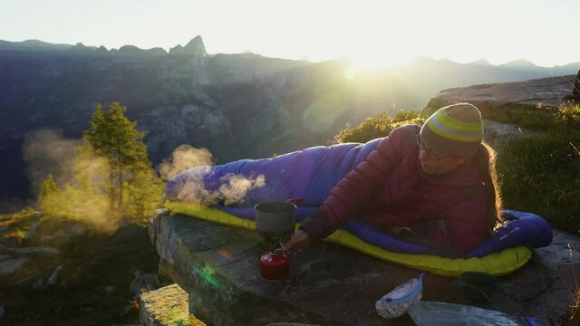 A woman making breakfast at her bivouac on a beautiful morning in the mountains.