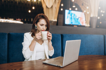 Beautiful Young Freelancer Woman Using Laptop Computer Sitting At Cafe Table. Happy Smiling Girl Working Online Or Studying And Learning While Using Notebook. Freelance Work, Business People Concept